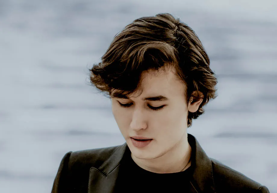 Person står framför en ljus bakgrund med mjuka horisontella linjer.