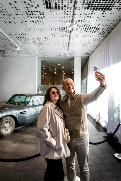 Par fotograferar selfie vid Aston Martin bilen i foajen