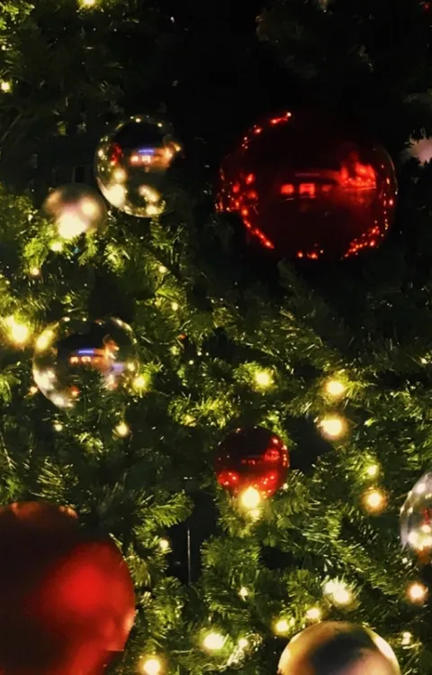 Röda, silvriga och guldiga julgranskulor hänger i en upplyst julgran 