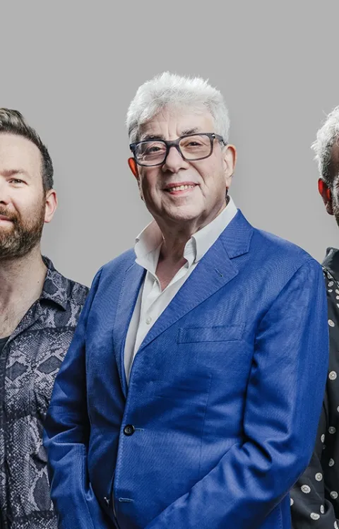 Fem personer från bandet 10cc ståendes framför en enfärgad bakgrund