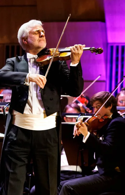 Orkester som framför musik på scen med en solist som spelar violin.