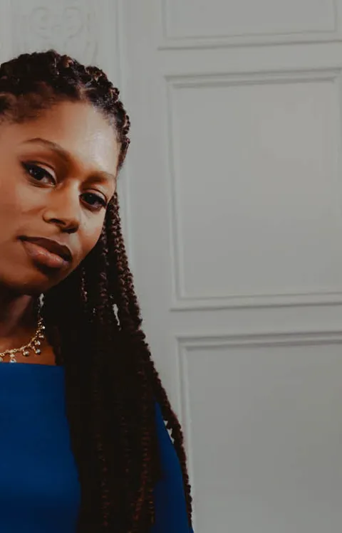 Person i blå klänning sitter vid ett piano och håller lila blommor framför vit panelvägg till konserten Stravinskij och Beethoven med Malmö Symfoniorkester.