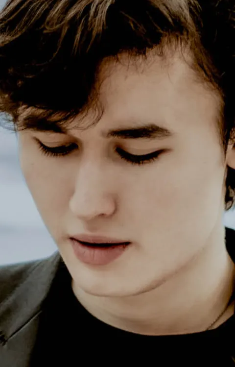 Person står framför en ljus bakgrund med mjuka horisontella linjer.