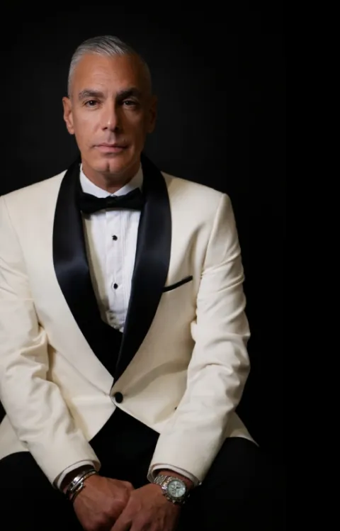 Shan Atci sittandes i kostym och fluga representerar showen