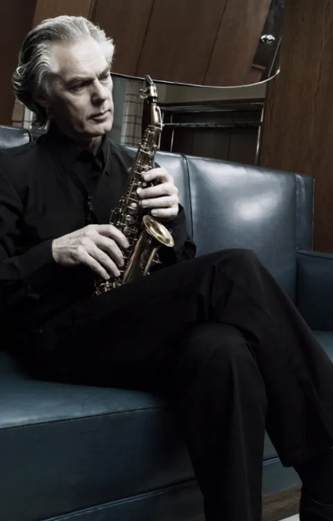 Porträtt av Jan Barbarek sittandes i en svart soffa med sin saxofon