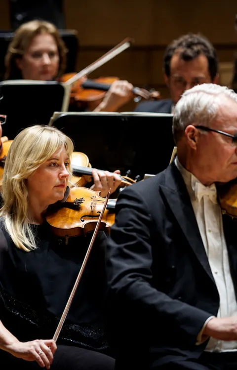Musiker från MSO symfoniorkester spelar stråkinstrument på scen under en konsert, med fokus på violinsektionen i förgrunden.