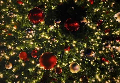 Röda, silvriga och guldiga julgranskulor hänger i en upplyst julgran 