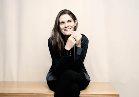 Kvinna med mörka kläder sitter framför en ljus vägg till konserten Beethovens sjua med Malmö Symfoniorkester.