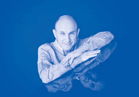 Person framför en blå bakgrund till konserten Brahms pianokonsert nr 1 med Malmö SymfoniOrkester.