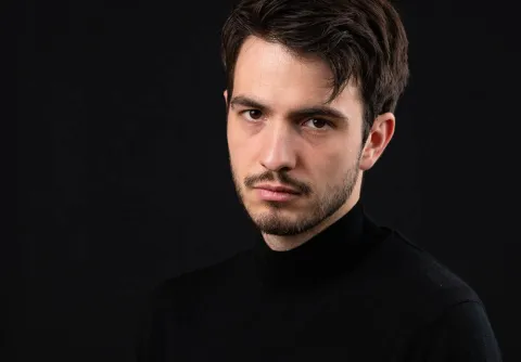 Man iklädd svart skjorta stående framför en vart bakgrund till konserten Bruckners åtta med Malmö Symfoniorkester.