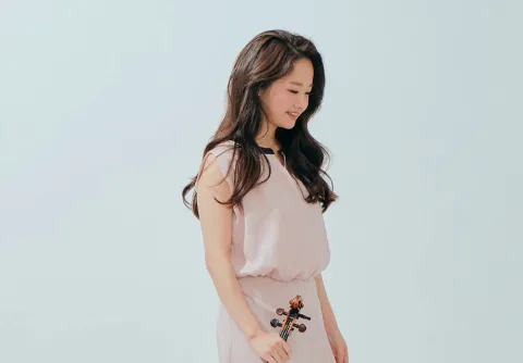 Kvinna håller en violin mot sidan i en ljus studio bakgrund till konserten Mendelssohns Violinkonsert med Malmö Symfoniorkester..