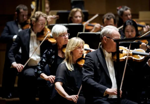 Musiker från mso symfoniorkester spelar stråkinstrument på scen under en konsert, med fokus på violinsektionen i förgrunden.